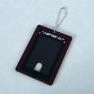 May include: A rectangular ID badge holder with a black interior and a red and black patterned border. The badge holder has a silver chain and the text "IT'S DANGEROUS TO GO ALONE! TAKE THIS." is printed on the top.