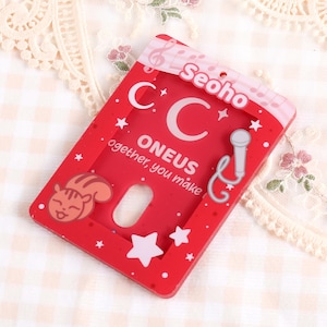 Könnte beinhalten: Ein roter Kunststoff-Kartenhalter mit dem Text "ONEUS together, you make" und dem Namen "Seoho". Der Halter zeigt einen Cartoon-Eichhörnchen, Sterne, Noten und eine Mikrofon-Grafik. Der Kartenhalter hat eine rechteckige Form mit abgerundeten Ecken.