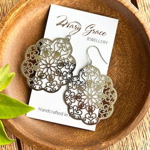 Könnte beinhalten: Ein Paar silberfarbene Filigranohrringe mit floralem Design. Die Ohrringe werden auf einer weißen Karte mit dem Text "Mary Grace Jewellery" und "Handcrafted in Australia" präsentiert. Die Ohrringe liegen in einer Holzschale.