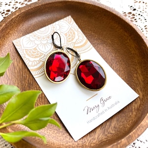 May include: Red gemstone earrings with a gold-coloured frame. The oval-shaped earrings have a lever-back closure. The earrings are displayed on a white card with the text "Mary Grace Handcrafted in Australia".