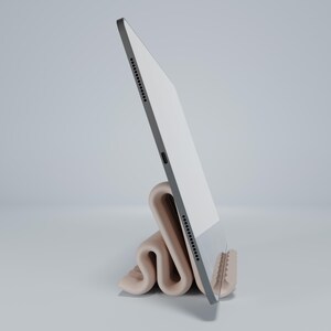 May include: A white tablet computer is propped up in a beige, folded stand. The tablet is in portrait mode and the stand is made of a soft, flexible material.