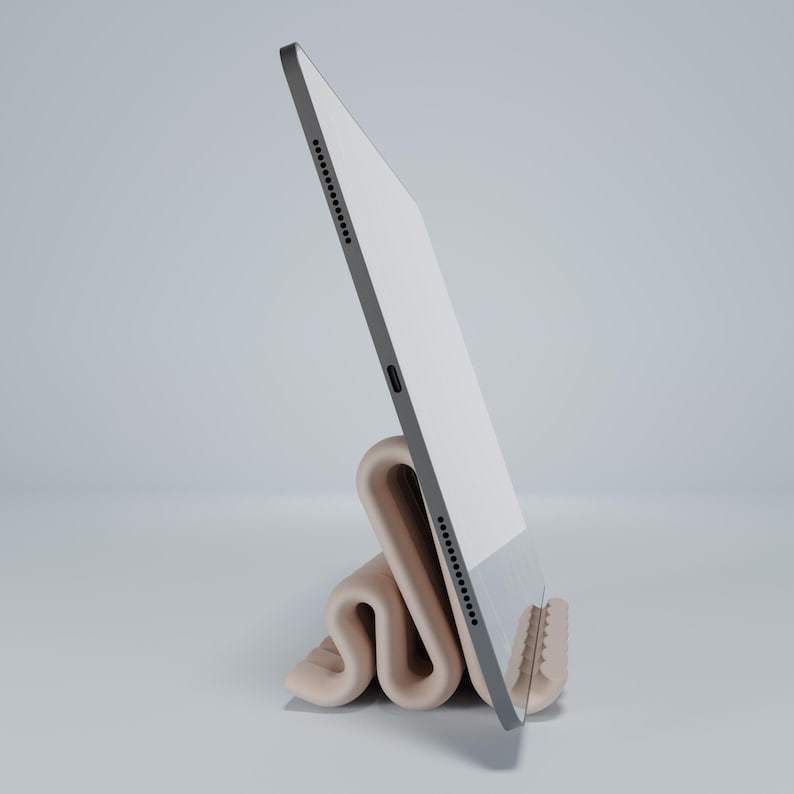 May include: A white tablet computer is propped up in a beige, folded stand. The tablet is in portrait mode and the stand is made of a soft, flexible material.