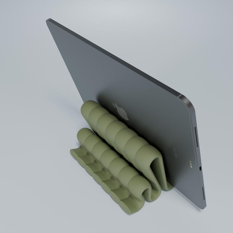 May include: A green, flexible, and foldable stand for a tablet or laptop. The stand is made of a soft, rubber-like material and has a series of ridges that create a stable base for the device. The stand is designed to prop up the device at an angle, making it easier to view and use.