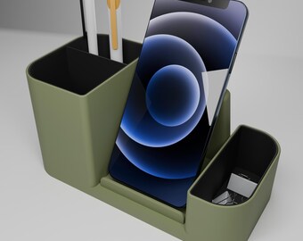 May include: Olive green desk organizer with compartments for pens, a smartphone, and small office supplies. The organizer holds a smartphone with a blue and black screen, two pens, and paper clips.