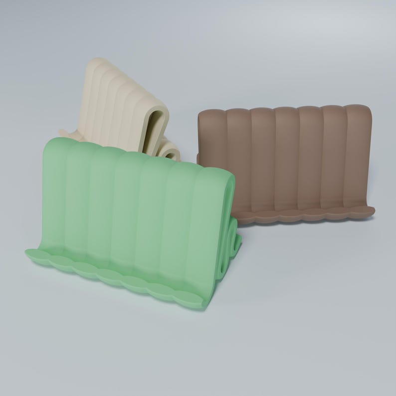 May include: Three phone stands made of a flexible, rubber-like material. The stands are in green, brown, and beige.