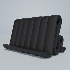 May include: Black phone stand made of flexible, ribbed material. The stand is shaped like a wave and has five slots for holding phones.
