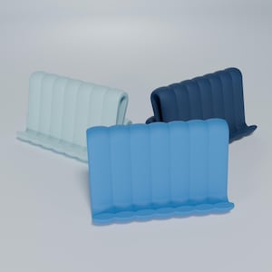 May include: Three phone stands made of silicone in different shades of blue. The stands are designed with a wavy, rippled texture.