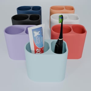 May include: A light blue toothbrush holder with two compartments, one holding a tube of toothpaste that says "Strong Teeth" and the other holding an electric toothbrush. The holder is surrounded by other toothbrush holders in various colors, including purple, black, orange, and white.