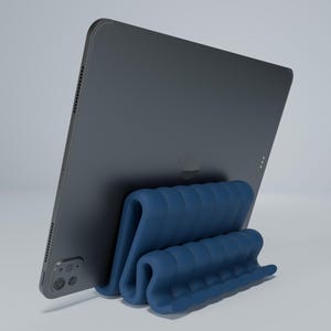 May include: A blue silicone stand for a tablet. The stand is shaped like a series of connected waves. A black tablet is resting on the stand.