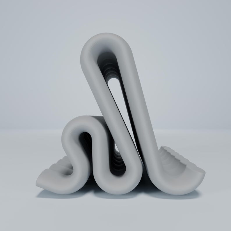 May include: A gray, folded, abstract sculpture made of a smooth, rubber-like material. The sculpture is folded into a series of loops and curves, creating a unique and interesting shape.