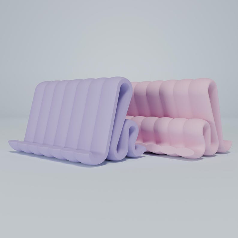 May include: Two phone stands made of a soft, flexible material. The stand on the left is lavender and the stand on the right is pink.