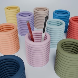 May include: A set of nine colorful, stacked, cylindrical pencil holders. The holders are in various colors, including blue, green, pink, orange, and yellow. Two pencils are in one of the holders.