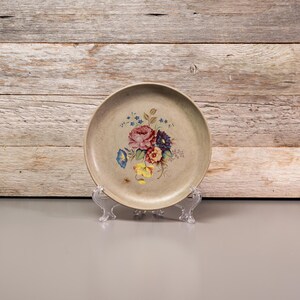 Peut inclure: Une assiette décorative avec un motif floral composé de fleurs roses, jaunes, bleues et violettes sur un fond beige.