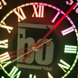 Può includere: Un quadrante di orologio nero con numeri romani e una lancetta rossa e bianca. Il quadrante dell'orologio è illuminato da un arcobaleno di colori, tra cui rosa, verde e blu. Il quadrante dell'orologio ha il testo "Jagermeister" attorno al bordo.