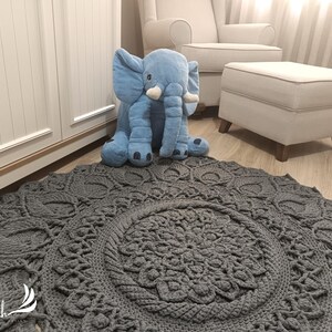 May include: A gray crocheted rug with a large circular pattern in the center. A blue plush elephant toy is sitting on the rug.