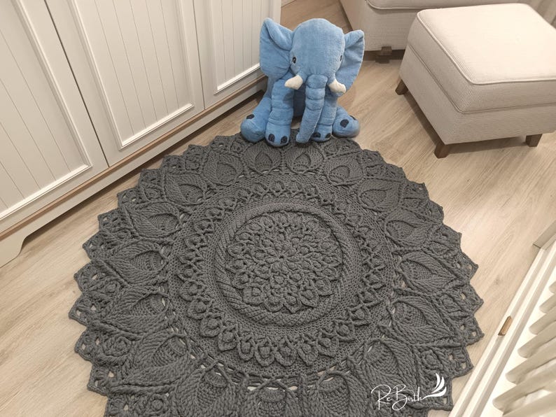 May include: A gray crocheted round rug with a large circular pattern in the center. The rug has a delicate, lacy design and is perfect for adding a touch of handmade charm to any room.