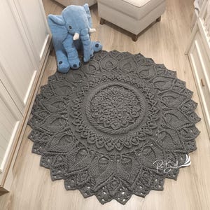 May include: A gray crocheted round rug with a mandala design. The rug has a large central circle with a smaller circle inside. The rug is on a wooden floor.