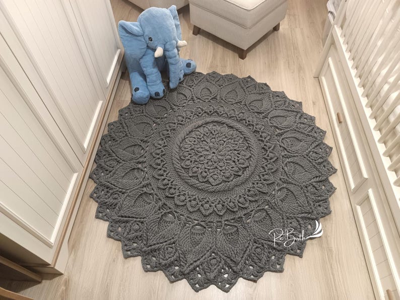 May include: A gray crocheted round rug with a mandala design. The rug has a large central circle with a smaller circle inside. The rug is on a wooden floor.