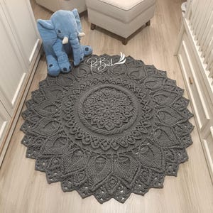 May include: A gray crocheted round rug with a mandala design. The rug has a delicate, intricate pattern and is perfect for adding a touch of bohemian style to any room.