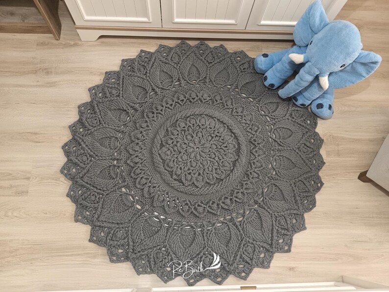 May include: A gray crocheted round rug with a mandala design. The rug has a delicate, intricate pattern with a central flower motif.
