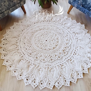 Könnte beinhalten: Ein großer, cremefarbener gehäkelter Teppich mit einem runden Mandala-Muster. Der Teppich hat ein zartes, durchbrochenes Muster und einen Fransenrand.