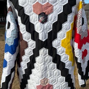 May include: A quilted jacket with a geometric pattern of white, black, yellow, and red hexagons. The jacket features a variety of fabric patterns, including floral and solid colors. The jacket has long sleeves and a unique, handcrafted design.