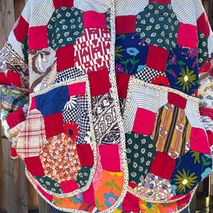 May include: A quilted jacket constructed from various fabric patches in diverse colors and patterns, including floral, plaid, gingham, and striped designs. The garment features a high collar, a front button closure, and two large patch pockets.