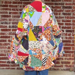 May include: A patchwork jacket with a vibrant mix of colors and patterns. The jacket features a variety of fabric pieces in red, yellow, blue, and floral prints, sewn together in a quilt-like design. The sleeves have ruffled edges, adding a decorative touch.