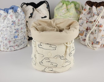 Può includere: Una collezione di cinque borse cilindriche trapuntate con coulisse, caratterizzate da vari motivi tra cui conigli bianchi su fondo crema, stampe animali colorate e interni a tinta unita. Ogni borsa ha una tasca frontale con chiusura a scatto.
