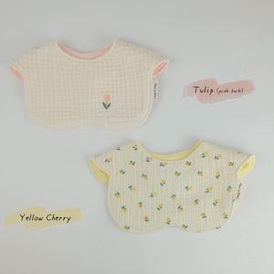 Pu&ograve; includere: Due bavaglini arrotondati per neonati in tessuto testurizzato. Il bavaglino superiore &egrave; color crema con un piccolo ricamo a tulipano e retro rosa. Il bavaglino inferiore presenta un motivo a ciliegie gialle con retro giallo. Entrambi hanno etichetta.