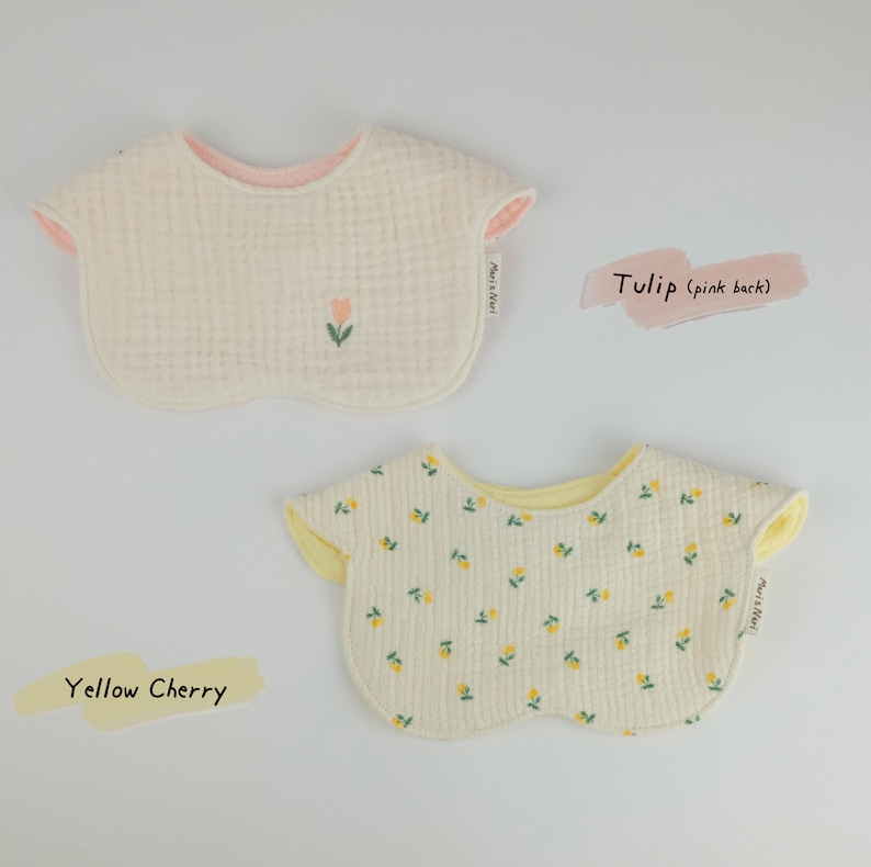 Pu&ograve; includere: Due bavaglini arrotondati per neonati in tessuto testurizzato. Il bavaglino superiore &egrave; color crema con un piccolo ricamo a tulipano e retro rosa. Il bavaglino inferiore presenta un motivo a ciliegie gialle con retro giallo. Entrambi hanno etichetta.