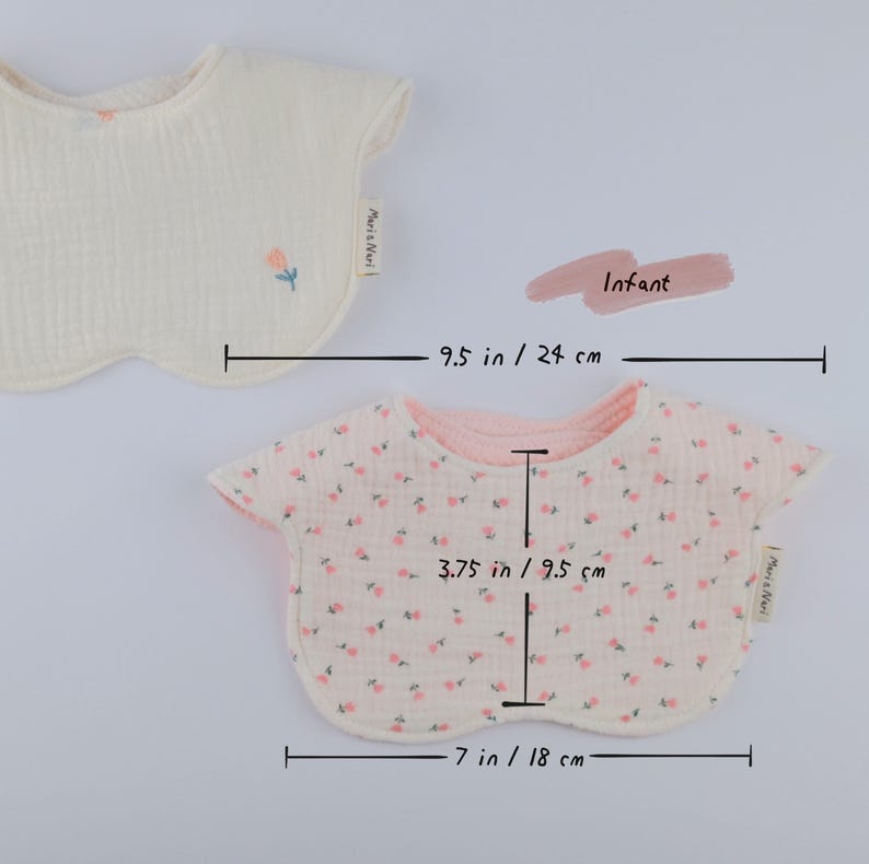 Pu&ograve; includere: Due bavaglini per neonati in tessuto testurizzato. Uno &egrave; color crema con un piccolo fiore ricamato e una larghezza di 24 cm. L'altro presenta un motivo floreale rosa, misura 18 cm di larghezza e 9,5 cm dal collo al bordo inferiore.