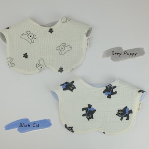 Pu&ograve; includere: Due bavaglini arrotondati con superficie in tessuto testurizzato. Il bavaglino superiore &egrave; bianco sporco con stampa di cuccioli grigi e fiori, etichettato Grey Puppy. Il bavaglino inferiore &egrave; bianco sporco con stampa di gatti neri con borse blu, etichettato Black Cat.