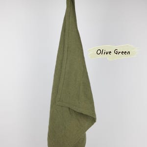 Puede incluir: Un pa&ntilde;o de cocina de color verde oliva con un lazo para colgar, drapeado sobre una rama de madera. La tela tiene una textura tejida visible. Un gr&aacute;fico rectangular de color claro a la derecha muestra el texto Olive Green en letras negras.