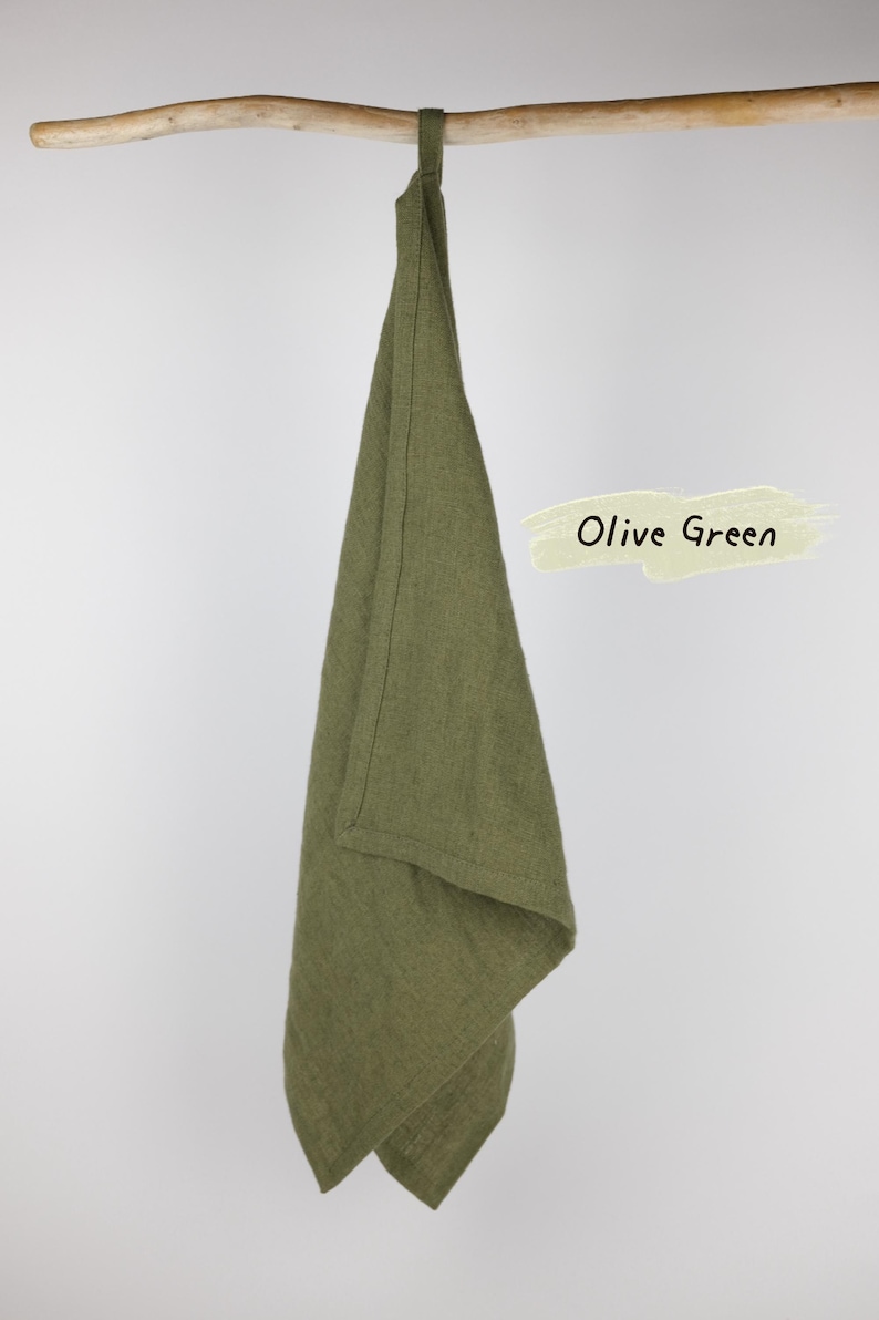 Puede incluir: Un pa&ntilde;o de cocina de color verde oliva con un lazo para colgar, drapeado sobre una rama de madera. La tela tiene una textura tejida visible. Un gr&aacute;fico rectangular de color claro a la derecha muestra el texto Olive Green en letras negras.