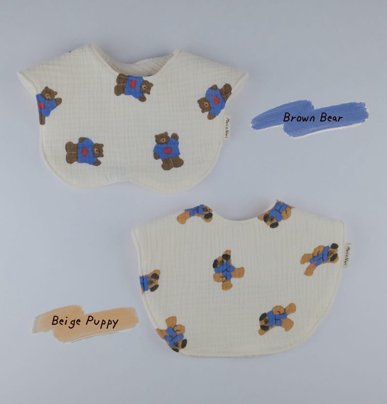 Pu&ograve; includere: Due bavaglini in tessuto color bianco sporco con superficie testurizzata. Uno presenta un motivo ripetuto di orsi bruni con camicie blu, etichettato Brown Bear. L'altro presenta un motivo ripetuto di cuccioli beige con camicie blu, etichettato Beige Puppy.
