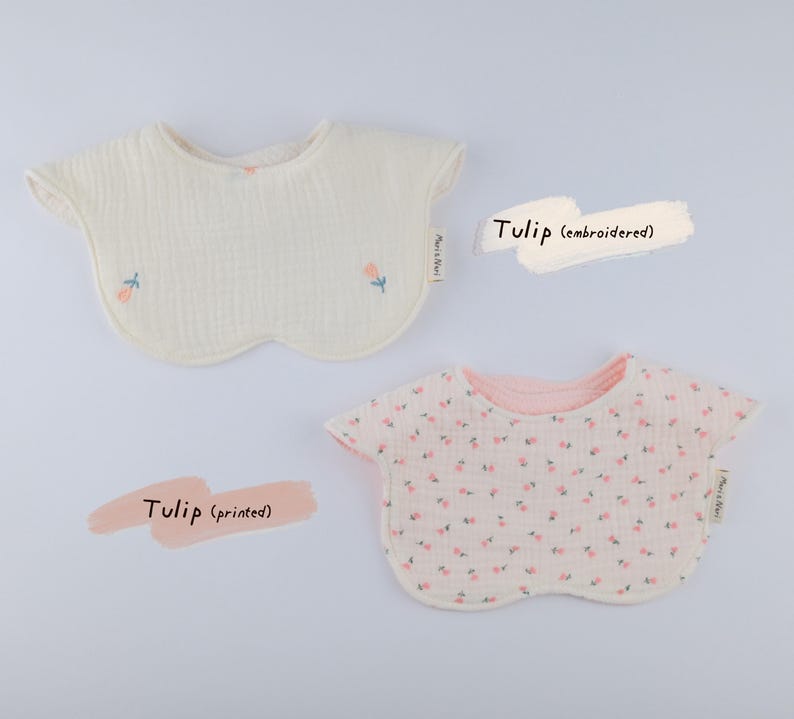 Pu&ograve; includere: Due bavaglini arrotondati per neonati in tessuto testurizzato. Uno &egrave; bianco sporco con piccoli tulipani rosa ricamati e steli verdi. L'altro &egrave; bianco con una fitta stampa di tulipani rosa. Entrambi hanno un'etichetta laterale Mari & Nui.