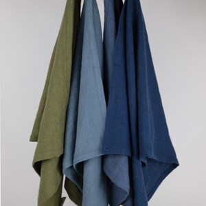 Puede incluir: Cuatro pa&ntilde;os de cocina rectangulares colgados de una barra de madera, cada uno con un lazo de tela en la parte superior. Los colores de izquierda a derecha est&aacute;n etiquetados como Olive Green, Muted Blue, Denim Blue y Navy Blue, con una etiqueta.