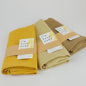 Puede incluir: Tres telas dobladas en tonos amarillo mostaza, beige claro y marr&oacute;n claro. Cada tela est&aacute; envuelta en una banda de papel beige con una etiqueta blanca con el texto I'm hand-made y un peque&ntilde;o gr&aacute;fico amarillo. Se adjunta una etiqueta blanca m&aacute;s peque&ntilde;a.