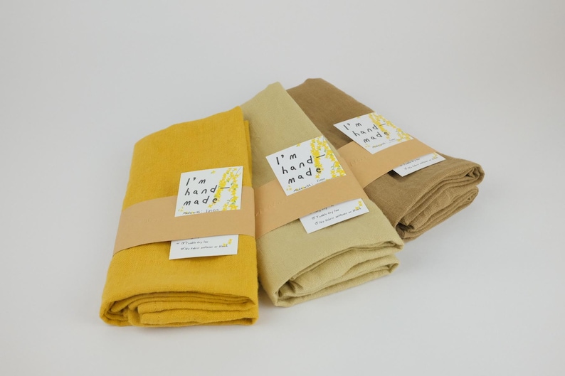 Puede incluir: Tres telas dobladas en tonos amarillo mostaza, beige claro y marr&oacute;n claro. Cada tela est&aacute; envuelta en una banda de papel beige con una etiqueta blanca con el texto I'm hand-made y un peque&ntilde;o gr&aacute;fico amarillo. Se adjunta una etiqueta blanca m&aacute;s peque&ntilde;a.