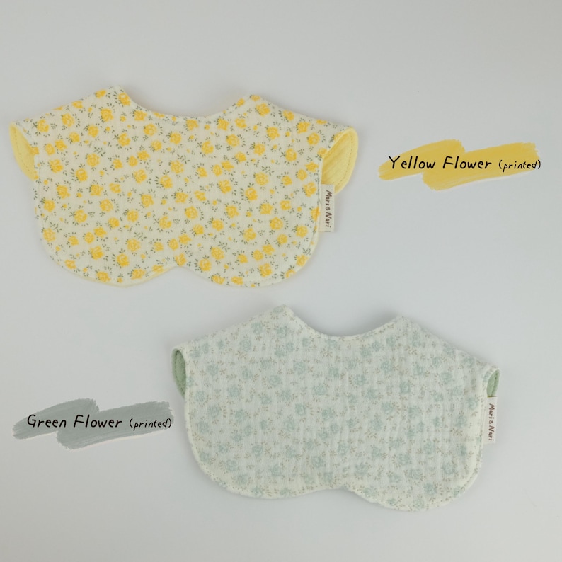 Pu&ograve; includere: Due bavaglini arrotondati con stampe floreali. Uno presenta un motivo a fiori gialli su sfondo bianco con retro giallo, l'altro un motivo a fiori verdi su sfondo bianco con retro verde. Entrambi sono dotati di un'etichetta Mari & Nari.