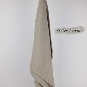Puede incluir: Un pa&ntilde;o de cocina rectangular hecho de tela de lino de color beige claro que cuelga de una rama de madera. El pa&ntilde;o cuenta con un peque&ntilde;o lazo de tela en la parte superior para colgarlo. El texto Natural Flax est&aacute; impreso en negro a la derecha.