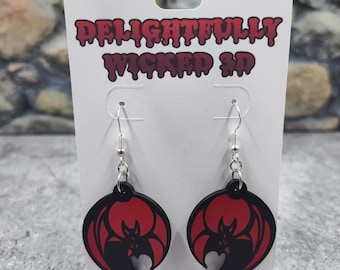 May include: A pair of black and red bat earrings with silver hooks. The earrings are on a white card with the text "Delightfully Wicked 3D".