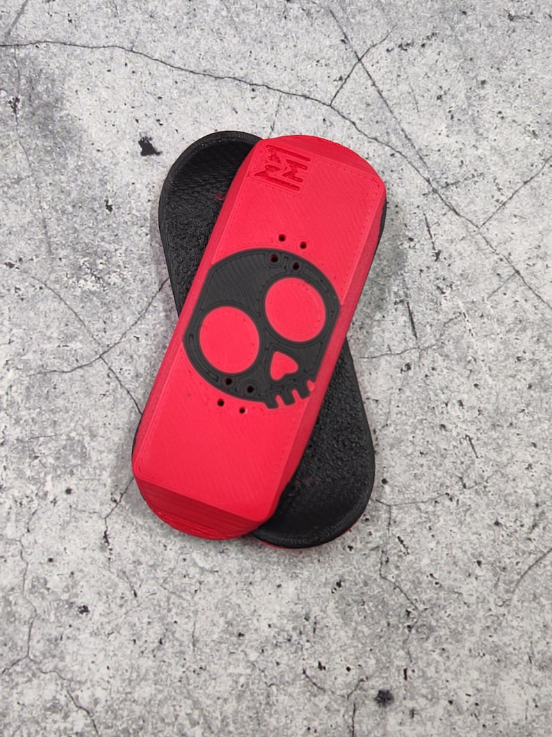 May include: A red and black fingerboard with a skull design. The fingerboard is red with a black skull graphic and black grip tape. The fingerboard is approximately 4 inches long.