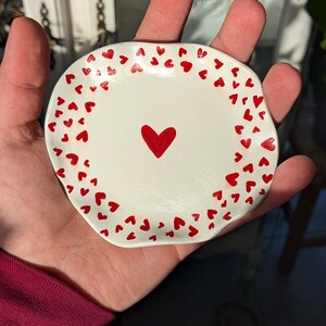 Peut inclure: Un plat en céramique blanche avec un cœur rouge au centre et une bordure de petits cœurs rouges.