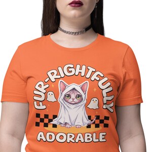 May include: Orange t-shirt with a graphic of a cat dressed as a ghost, with the words "FUR-RIGHTFULLY ADORABLE". The cat has big green eyes and is wearing a white sheet. Two small ghost figures are also in the design.