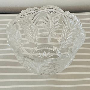 Peut inclure: Un bol en verre transparent d&eacute;coratif avec un bord festonn&eacute; et des motifs grav&eacute;s de feuilles et d'&eacute;clats d'&eacute;toiles. Le bol a une petite base circulaire avec un motif en forme d'&eacute;toile. Le bol est pos&eacute; sur une surface &agrave; rayures grises et blanches.
