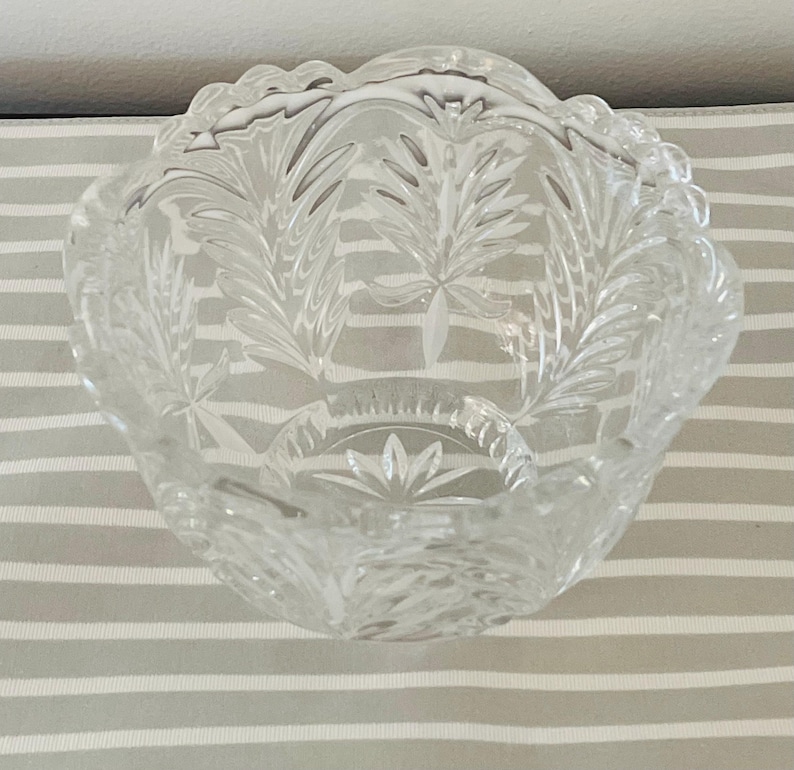 Peut inclure: Un bol en verre transparent d&eacute;coratif avec un bord festonn&eacute; et des motifs grav&eacute;s de feuilles et d'&eacute;clats d'&eacute;toiles. Le bol a une petite base circulaire avec un motif en forme d'&eacute;toile. Le bol est pos&eacute; sur une surface &agrave; rayures grises et blanches.