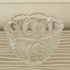 Peut inclure: Bol en verre transparent avec un bord festonn&eacute; et un motif de feuilles d&eacute;taill&eacute;. Le bol est rond et repose sur une surface ray&eacute;e. Le verre est transparent, laissant passer la lumi&egrave;re.