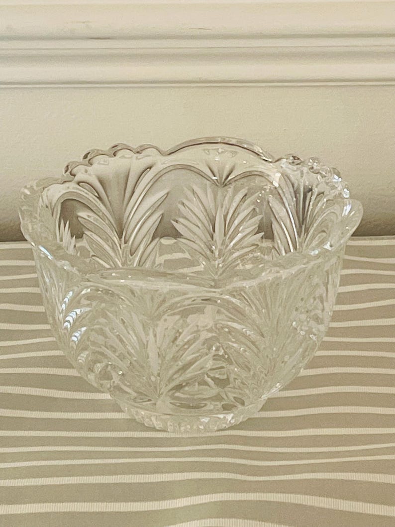 Peut inclure: Bol en verre transparent avec un bord festonn&eacute; et un motif de feuilles d&eacute;taill&eacute;. Le bol est rond et repose sur une surface ray&eacute;e. Le verre est transparent, laissant passer la lumi&egrave;re.
